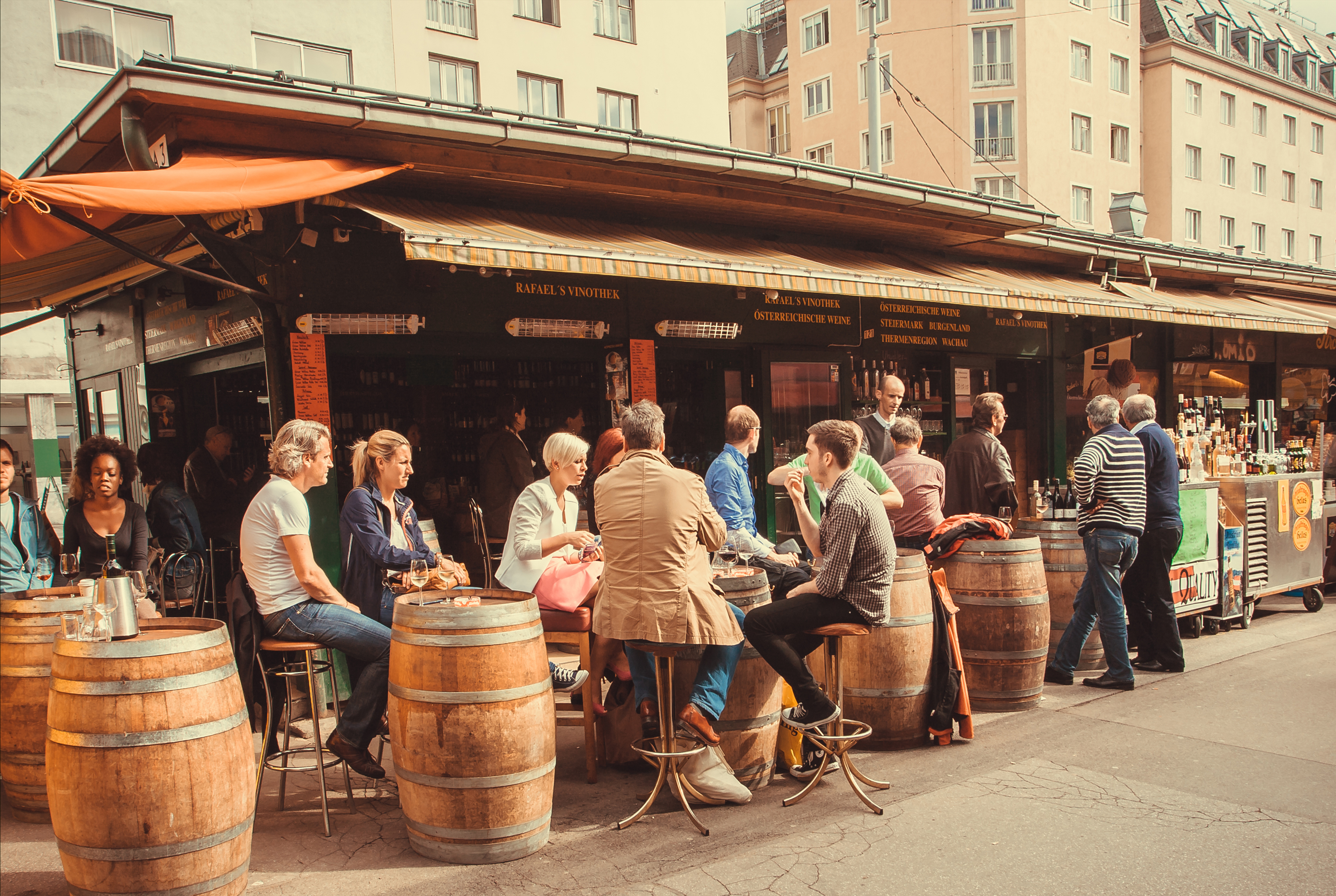Barrels like tables and people around in cafe or bar in outdoor area of Naschmarkt, popular market of the city of Vienna, Austria.